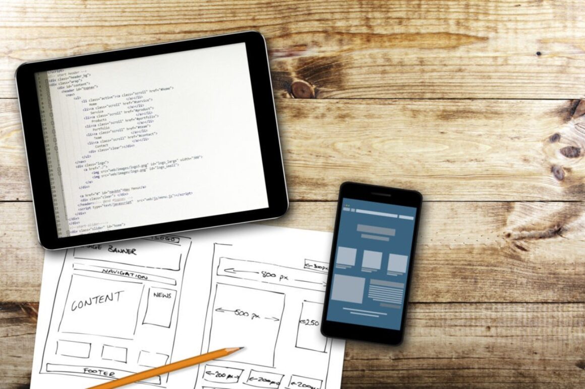 html coding on a tablet with website design sketches on paper