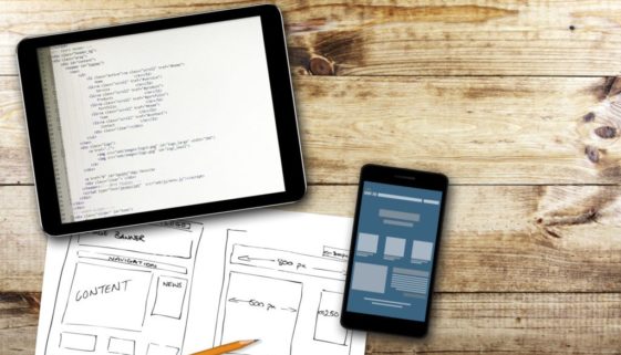 html coding on a tablet with website design sketches on paper