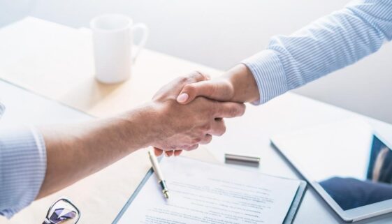 A business professional shaking hands with a client in an office space.