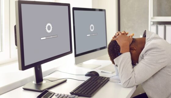 Man lays head on desk while computer website loads slowly.