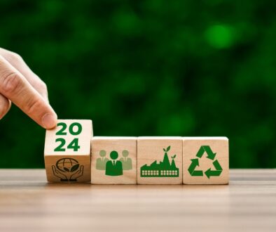 A hand tilting one of four wooden blocks with green sustainability symbols of them.